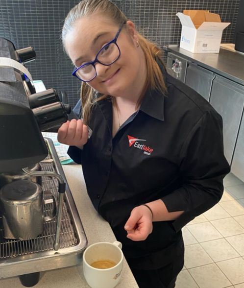 Charlotte smiling standing behind a coffee machine with a coffee cup on the table