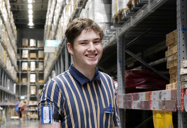 Brayden in his Ikea uniform smiling standing in warehouse