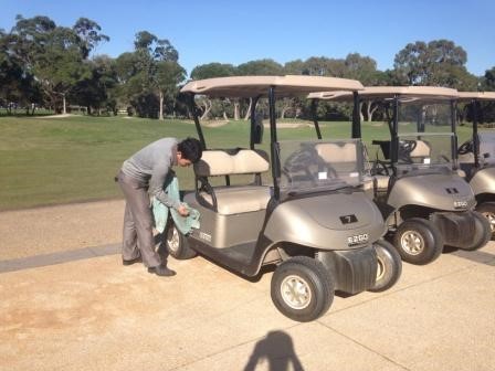 young man outside at a golf course cleaning a golf cart