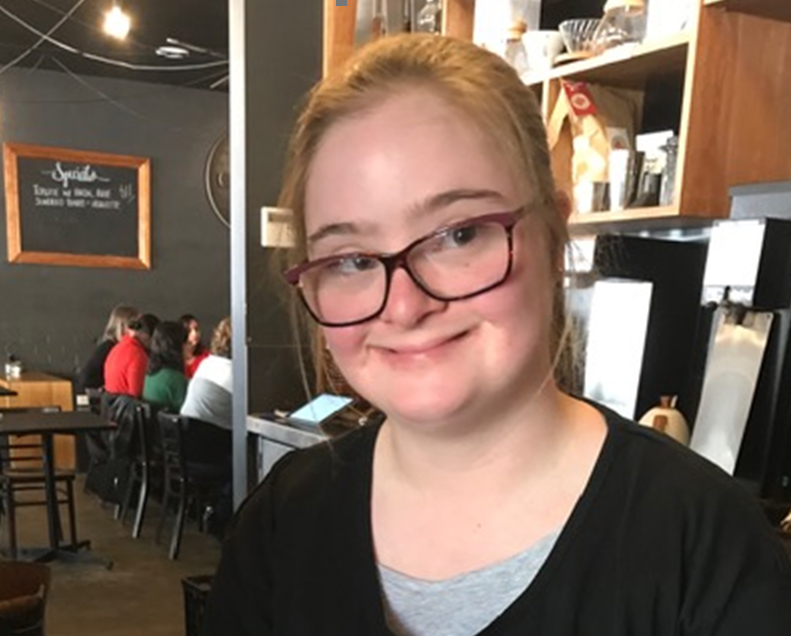 Charlotte smiling in a restaurant. Charlotte has glasses and is wearing black